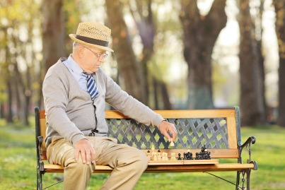 older man playing chess on bench lonely